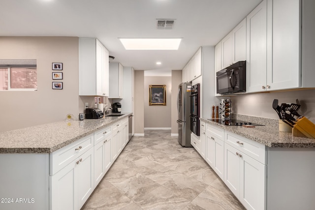 kitchen with kitchen peninsula, light stone counters, white cabinets, and black appliances