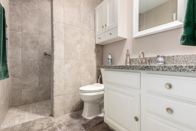 bathroom with vanity, toilet, a tile shower, and tile walls