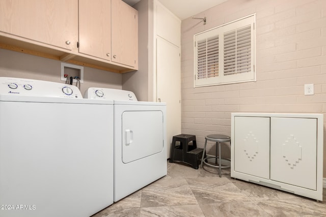 laundry area featuring washing machine and dryer, cabinets, and brick wall