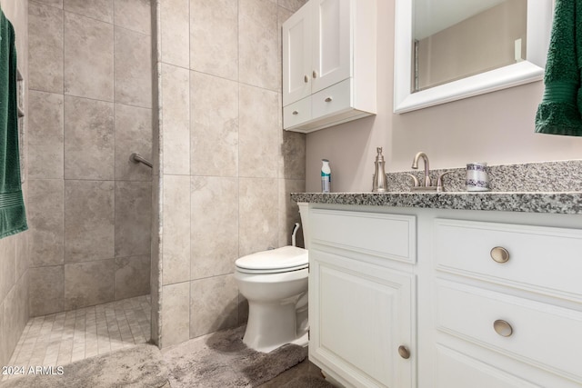 bathroom with tiled shower, vanity, toilet, and tile walls