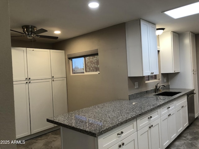 kitchen with stainless steel dishwasher, ceiling fan, sink, dark stone countertops, and white cabinetry