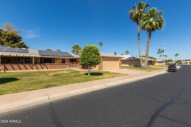 ranch-style home with solar panels, a garage, and a front lawn