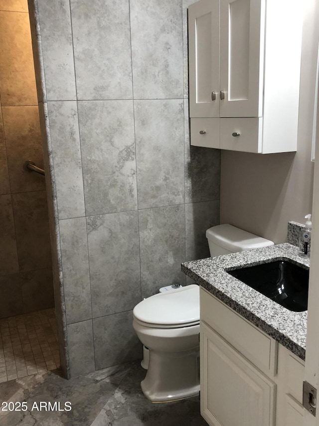 bathroom featuring walk in shower, vanity, toilet, and tile walls