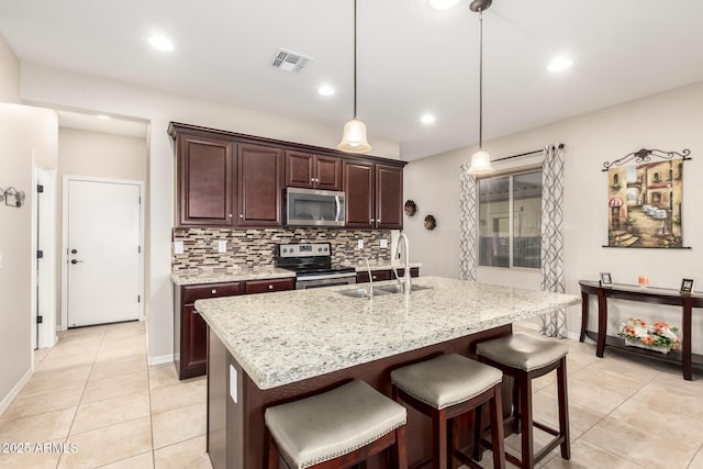 kitchen with a kitchen island with sink, sink, tasteful backsplash, decorative light fixtures, and stainless steel appliances