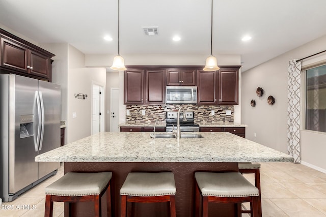 kitchen with appliances with stainless steel finishes, tasteful backsplash, sink, decorative light fixtures, and a center island with sink