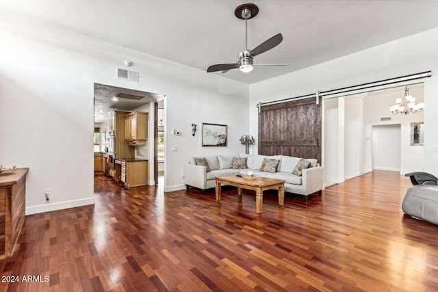 living room featuring dark hardwood / wood-style floors, a barn door, and ceiling fan with notable chandelier