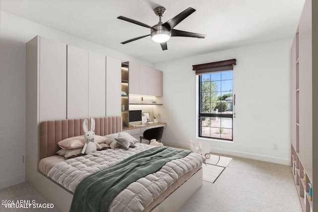 bedroom with built in desk, ceiling fan, and light colored carpet