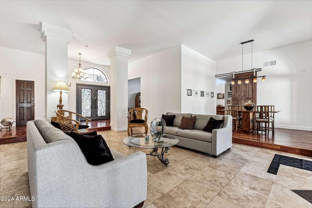 living room featuring french doors, ornate columns, a towering ceiling, and an inviting chandelier