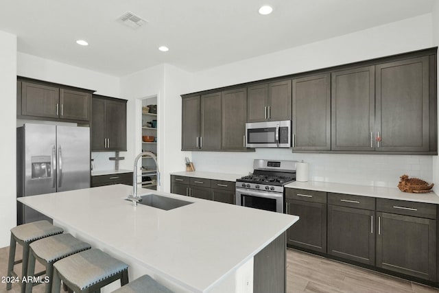 kitchen featuring sink, stainless steel appliances, a kitchen breakfast bar, an island with sink, and light wood-type flooring