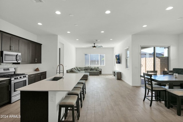 kitchen featuring a kitchen bar, ceiling fan, a kitchen island with sink, sink, and range with gas stovetop