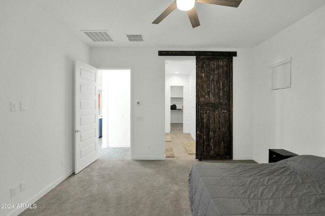 carpeted bedroom featuring a barn door and ceiling fan