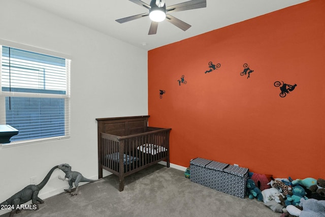 bedroom featuring a nursery area, light colored carpet, and ceiling fan