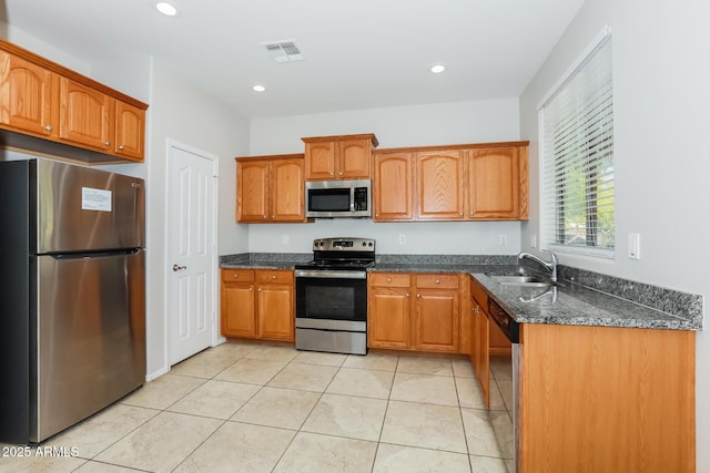 2475 E Vermont Dr, Gilbert, AZ 85295 - kitchen with appliances with stainless steel finishes, a sink, dark stone countertops, brown cabinetry, and light tile patterned floors