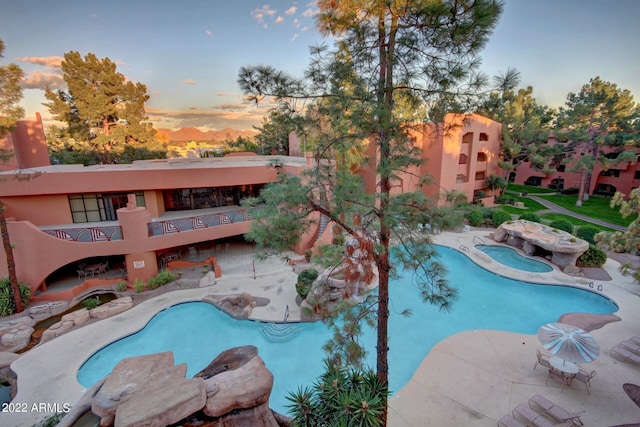 pool at dusk featuring a patio and an in ground hot tub