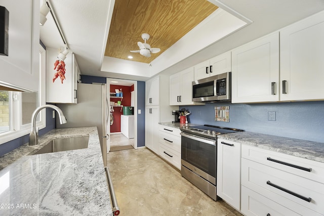 kitchen with white cabinets, a raised ceiling, appliances with stainless steel finishes, a sink, and light stone counters