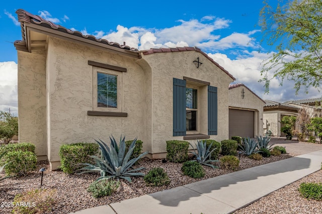 mediterranean / spanish home featuring stucco siding, an attached garage, a tile roof, and driveway
