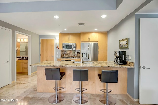 kitchen with a kitchen bar, light brown cabinets, kitchen peninsula, stainless steel appliances, and light stone countertops