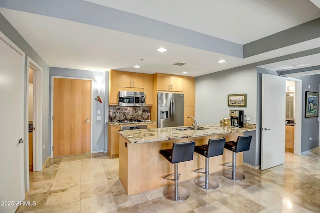 kitchen with sink, stainless steel appliances, light stone countertops, light brown cabinetry, and decorative backsplash