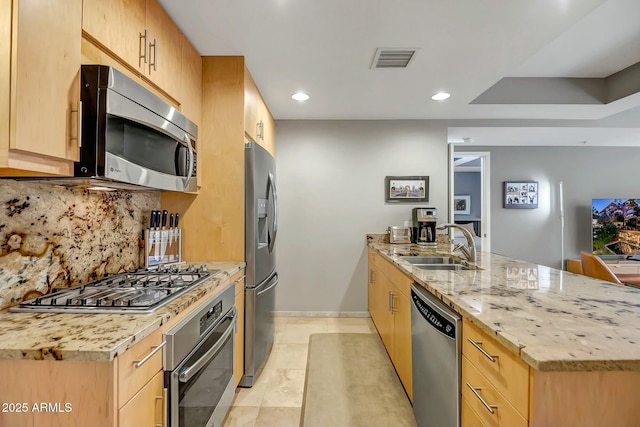 kitchen with light brown cabinetry, sink, light stone counters, stainless steel appliances, and decorative backsplash