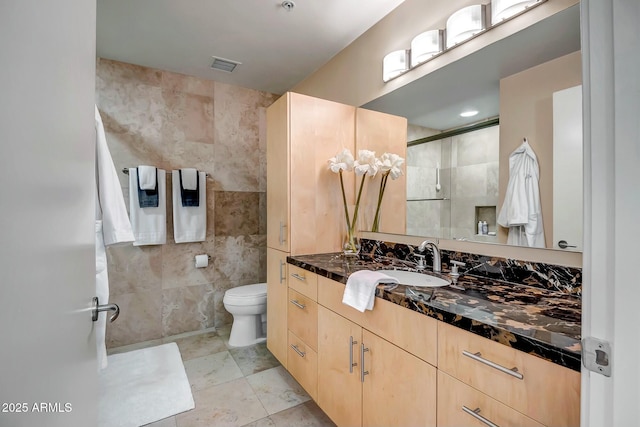 bathroom featuring vanity, toilet, and tile walls