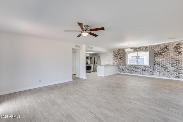 unfurnished living room featuring ceiling fan with notable chandelier, brick wall, light wood-type flooring, and sink