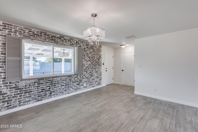 empty room featuring brick wall, a notable chandelier, and light hardwood / wood-style floors