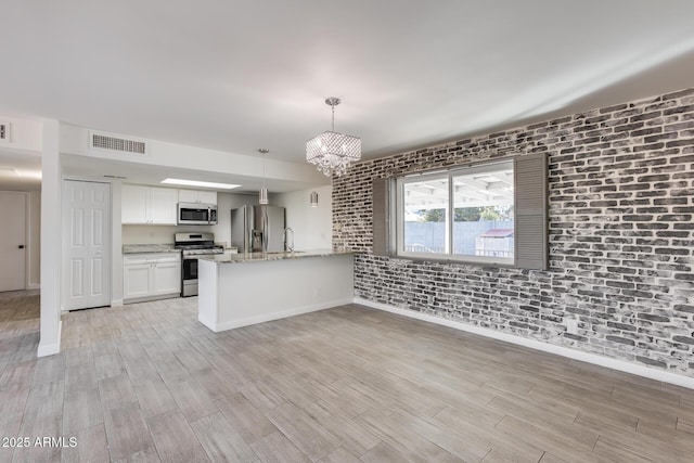 kitchen featuring stainless steel appliances, white cabinets, an inviting chandelier, decorative light fixtures, and brick wall