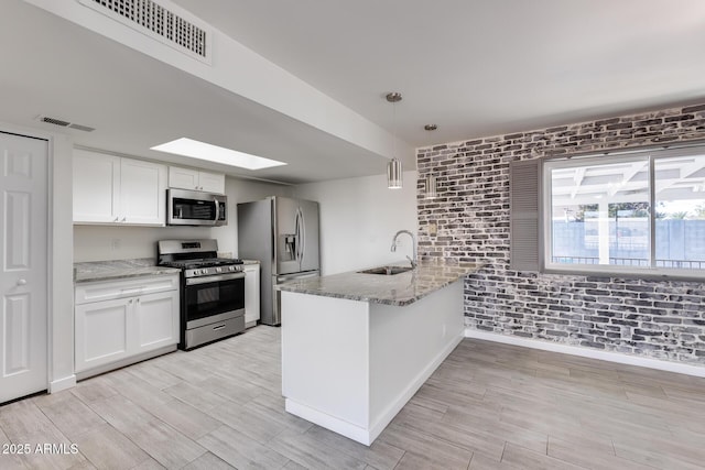 kitchen with hanging light fixtures, stainless steel appliances, brick wall, white cabinets, and sink