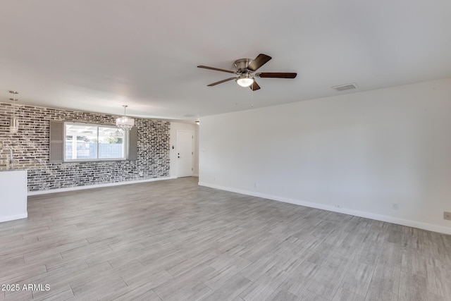 unfurnished room featuring ceiling fan with notable chandelier, light hardwood / wood-style flooring, and brick wall