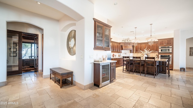 kitchen featuring a breakfast bar, decorative light fixtures, a center island, beverage cooler, and light stone countertops