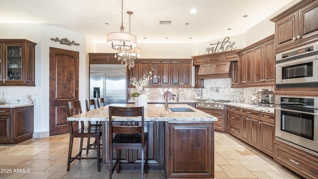 kitchen with sink, tasteful backsplash, hanging light fixtures, a center island with sink, and stainless steel appliances