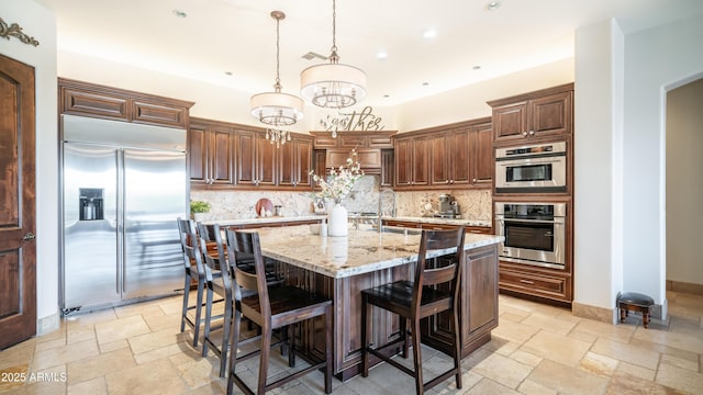 kitchen with tasteful backsplash, light stone counters, decorative light fixtures, a center island, and stainless steel appliances