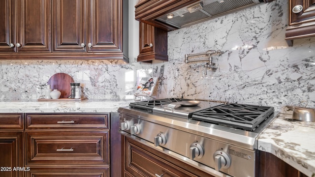 kitchen with dark brown cabinetry, stainless steel gas cooktop, custom range hood, light stone countertops, and decorative backsplash