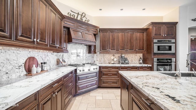 kitchen featuring sink, stovetop, premium range hood, light stone countertops, and decorative backsplash