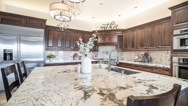 kitchen with sink, a breakfast bar area, light stone counters, decorative light fixtures, and appliances with stainless steel finishes