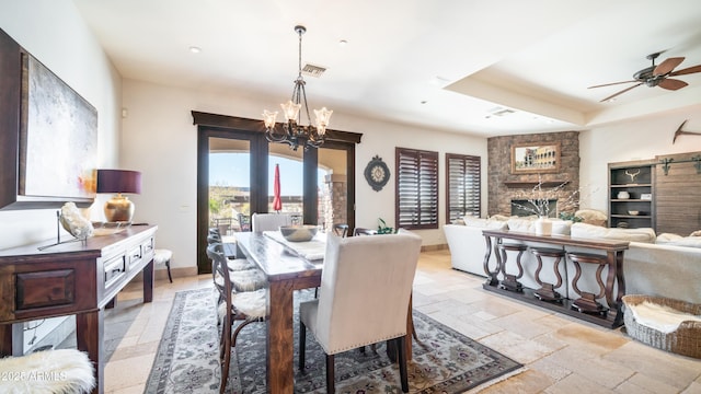 dining room featuring a fireplace, a raised ceiling, and ceiling fan with notable chandelier