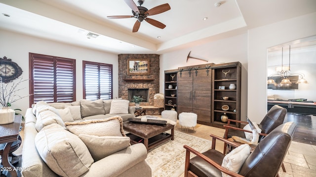 living room featuring a stone fireplace, ceiling fan, and a tray ceiling