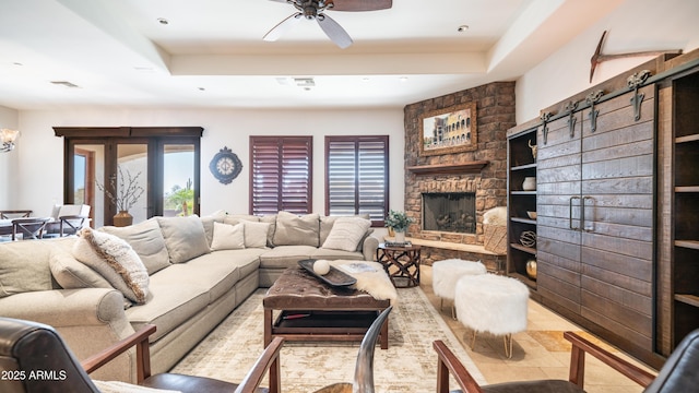 living room with ceiling fan, a barn door, a fireplace, and a tray ceiling