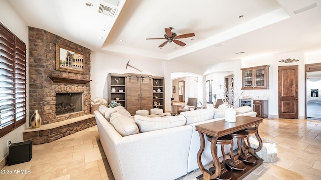 living room with a raised ceiling, ceiling fan, plenty of natural light, and a fireplace