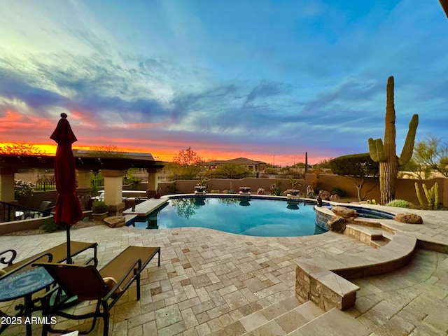 pool at dusk with a patio area and an in ground hot tub