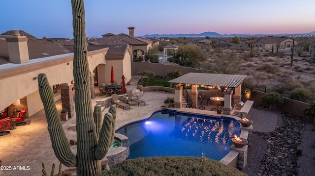 pool at dusk with an outdoor bar, a gazebo, a patio, pool water feature, and an in ground hot tub