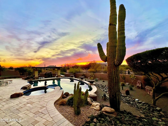 pool at dusk with a patio and an in ground hot tub