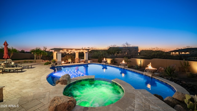 pool at dusk with an outdoor fire pit, a patio area, pool water feature, and an in ground hot tub