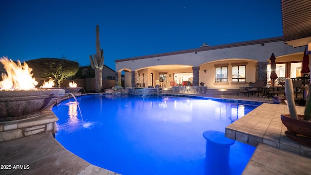 pool at twilight with an outdoor fire pit, pool water feature, and a patio area