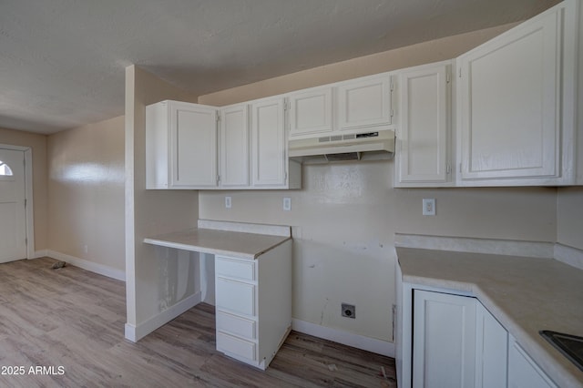 kitchen featuring under cabinet range hood, baseboards, light countertops, light wood-type flooring, and a textured ceiling