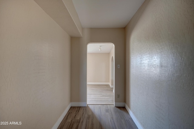 corridor featuring wood finished floors, baseboards, and arched walkways