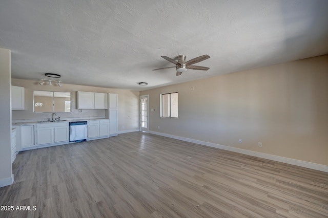 unfurnished living room with ceiling fan, baseboards, light wood-type flooring, a textured ceiling, and a sink