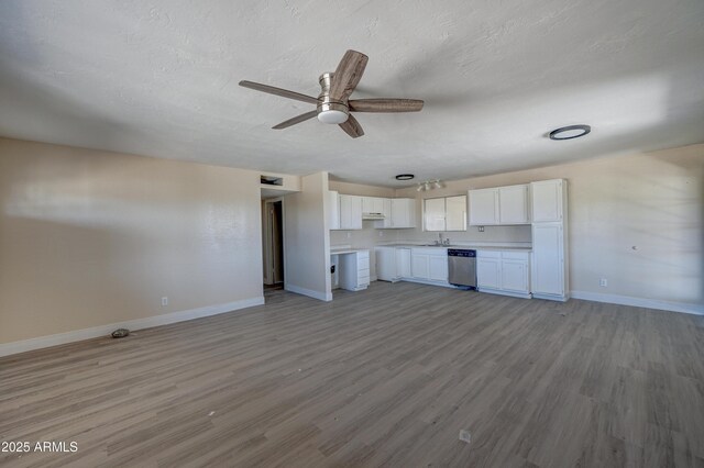 unfurnished living room with baseboards, ceiling fan, a sink, light wood-style floors, and a textured ceiling