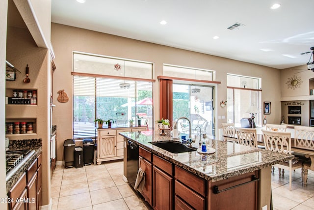 kitchen with light tile patterned flooring, stainless steel gas stovetop, an island with sink, sink, and light stone counters