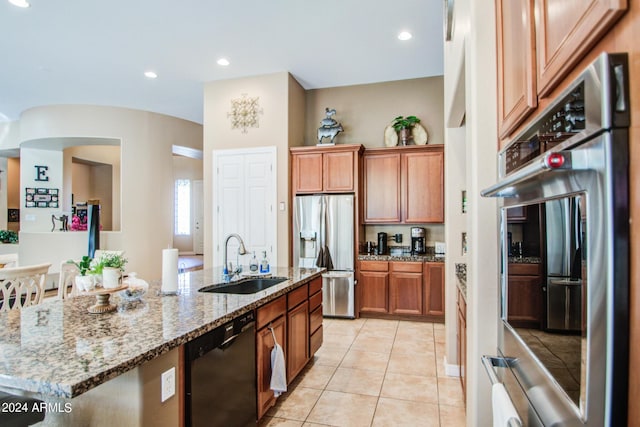 kitchen featuring sink, appliances with stainless steel finishes, light stone counters, an island with sink, and light tile patterned flooring